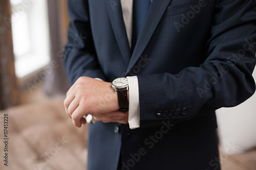 The groom in dark suit puts on a watch, closeup