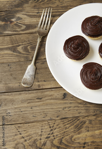 A plate of birthday cupcakes with chocolate frosting on a rustic wooden background with an antique silver fork