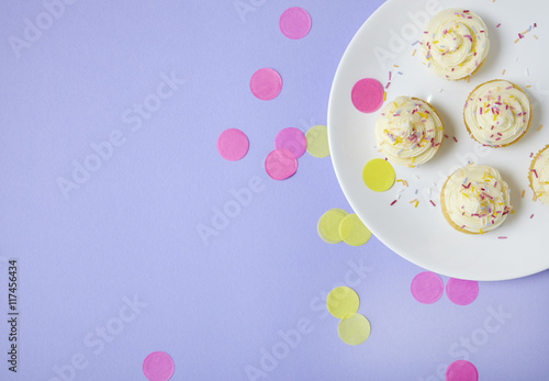 Cupcakes with vanilla frosting and sprinkles on a purple background with confetti forming a page border photo