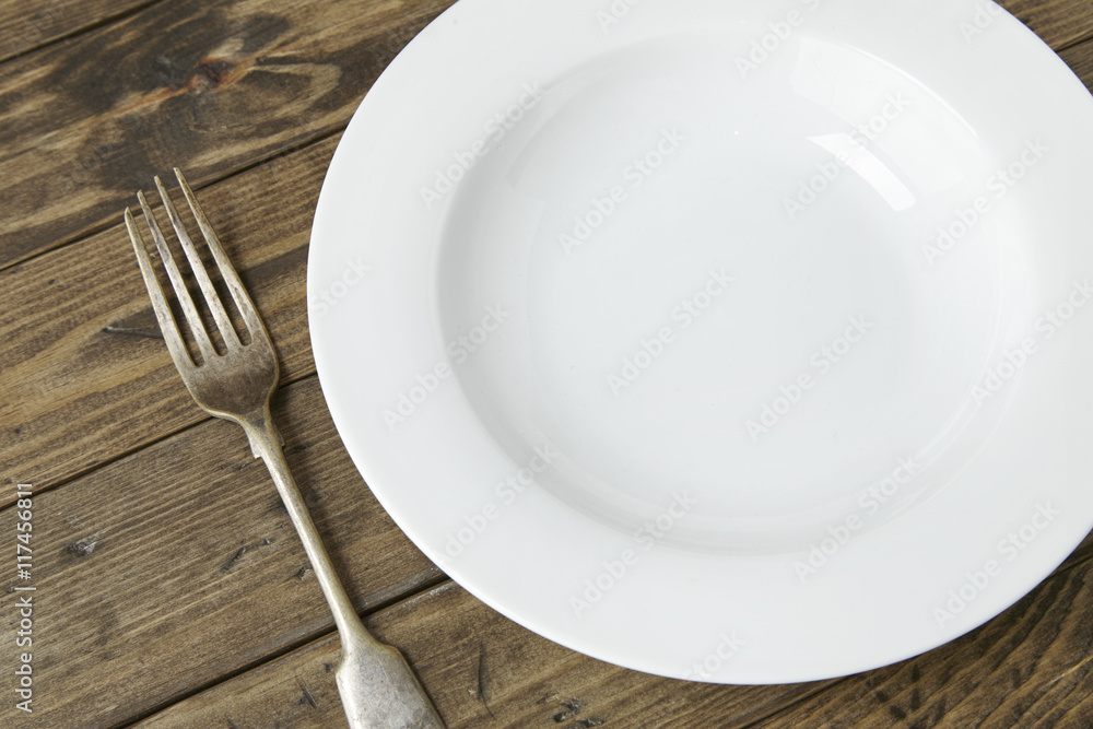 An empty white dinner plate and fork on a reclaimed wooden background