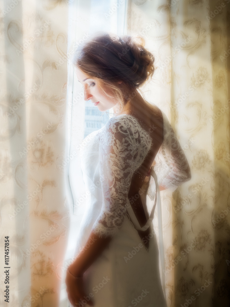 Fototapeta premium a beautiful bride posing in the early morning at the window, soaking up the first rays of the sun