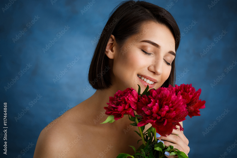 Close up portrait of tender young girl with red flowers over blue background Close up portrait of tender young girl with red flowers over blue background