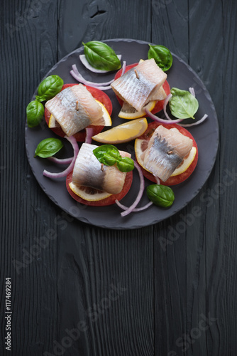 Canapes with herring on a black wooden background, above view