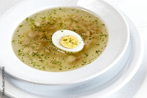 Low-fat chicken broth with a half cooked egg in a bowl isolated on white background