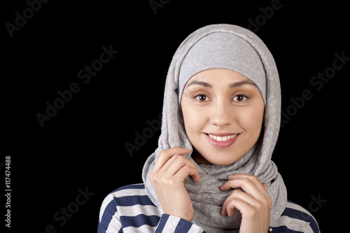 Portrait of a smiling young girl eastern appearance, with his head covered in a Muslim-style on a black background
