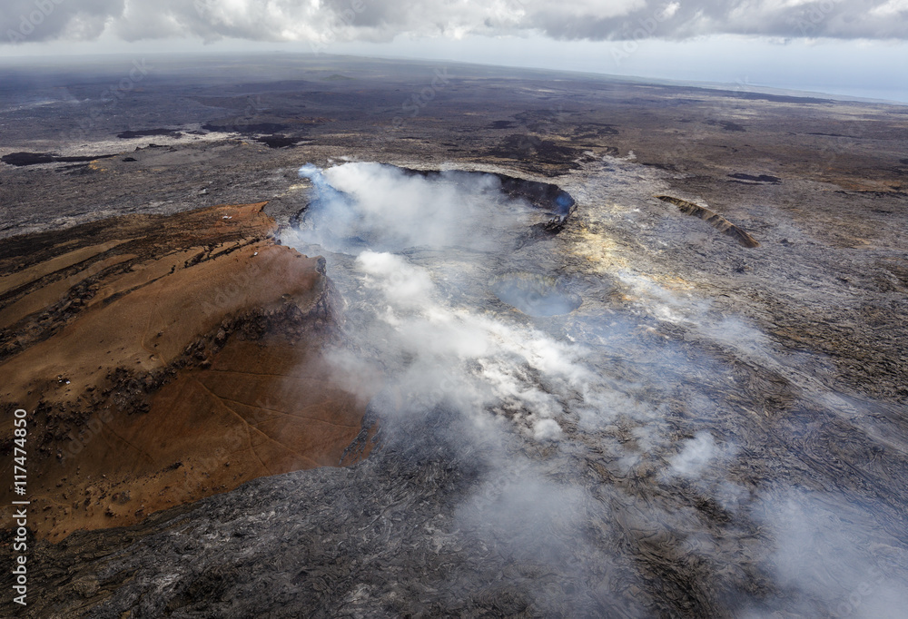 Smoking caldera of the Puu Oo vent with smaller crater in the foreground, Big Island, Hawaii. The lava field created by Puu Oo is in the background. Aerial photograph out of a helicopter.