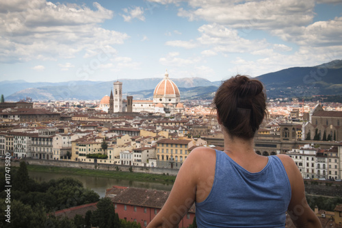 Girl looking over the historical center of Florence in Italy. The photo is taken from piazzale Michelangelo and shows the Arno river, the Duomo and many other churches and buildings 