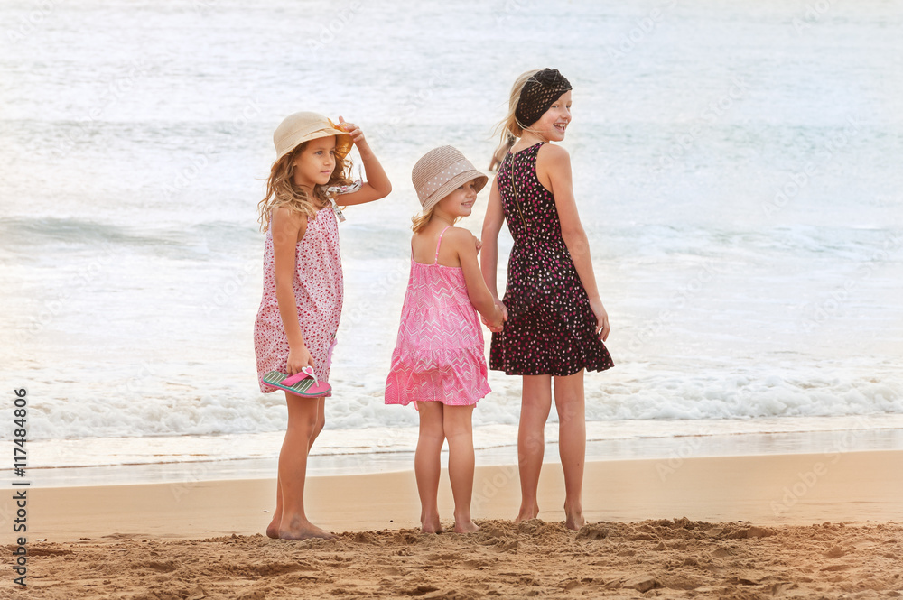 3 sisters stand on beachfront looking back at a person on the sh