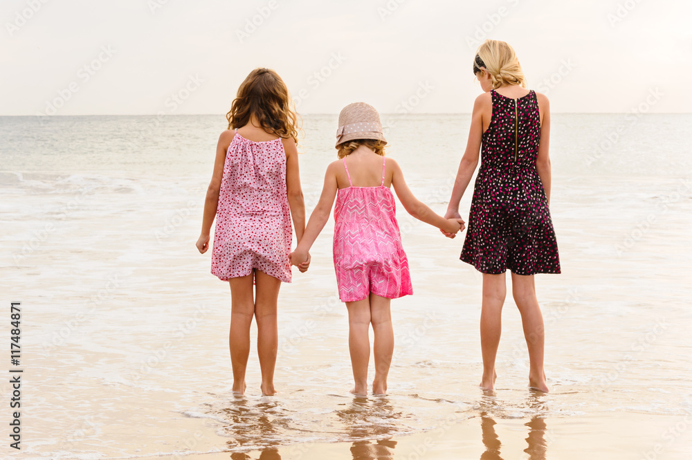 3 sisters stand on beachfront facing the ocean.