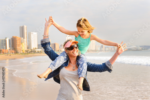 Young girl sitting on mom's shoulder while walking on beachfront