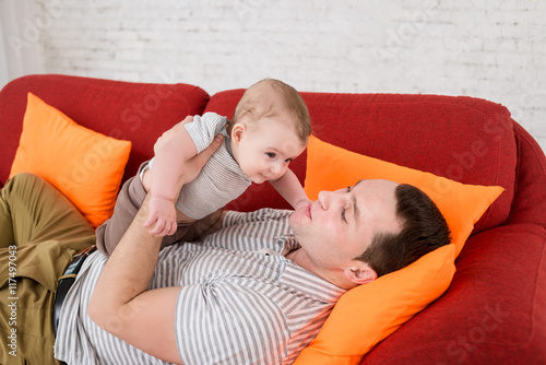 Fotografie father lays on the red sofa and holds little son