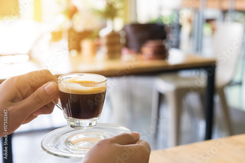 Woman hand holding hot espresso shot at coffee shop.