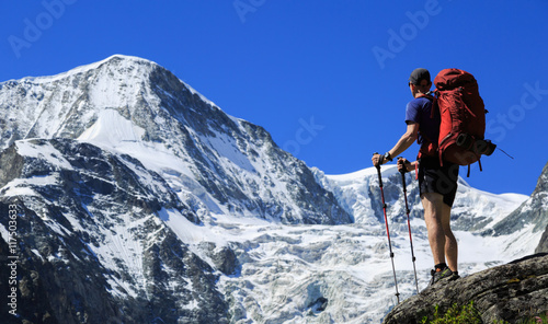 Hiker with backpack looking at mountain Pigne d' Arolla in Wallis, Switzerland, on a summers day.