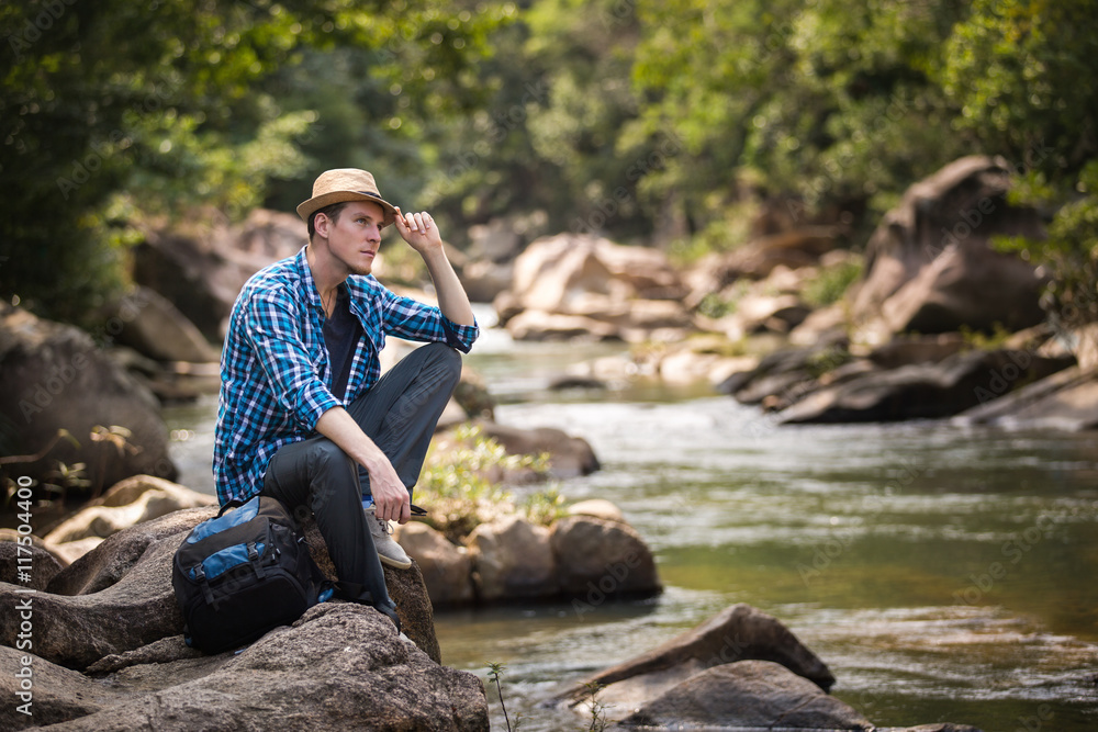 Male traveler sitting on the stone near river in jungle forest Male traveler sitting on the stone near river in jungle forest