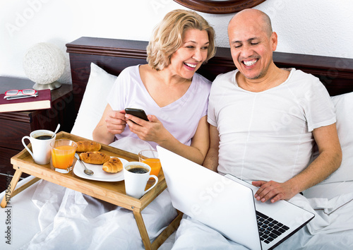 Mature positive smiling couple reading news from notebook photo