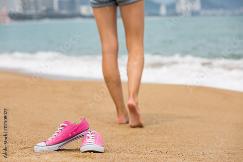 Woman walking barefoot on the beach, shoes in focus, shallow DOF