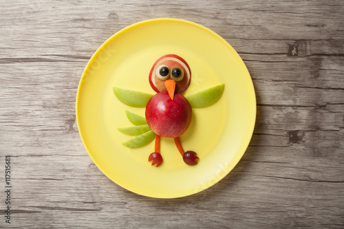 Funny bird made of apple on plate and wooden background