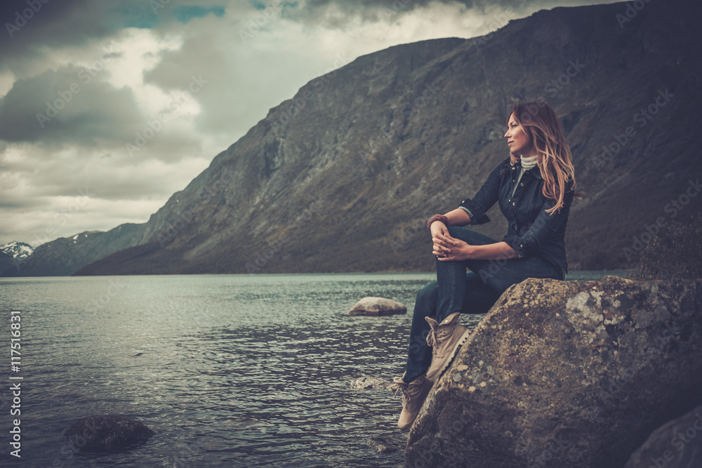 Beautiful woman posing on the shore of a wild lake, with mountains on the background. Beautiful woman posing on the shore of a wild lake, with mountains on the background.