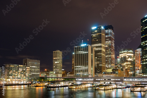 Circular Quay railway, train station and ferry wharfs with Sydney Central Business District cityscape skyscrapers at the background. Night shot, long exposure, copy space