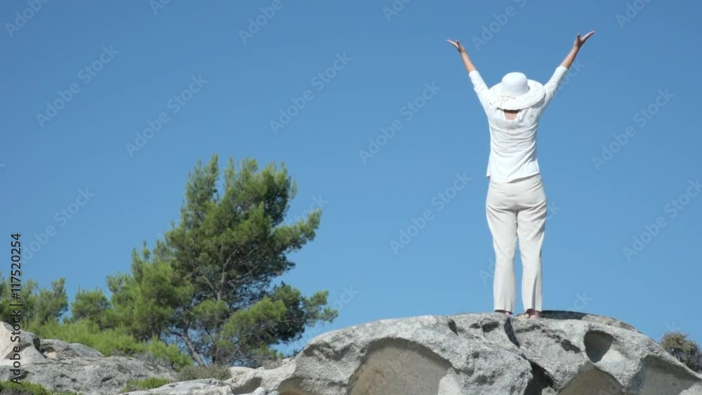 Woman with hands up standing on the hill near the sea Woman with hands up standing on the hill near the sea