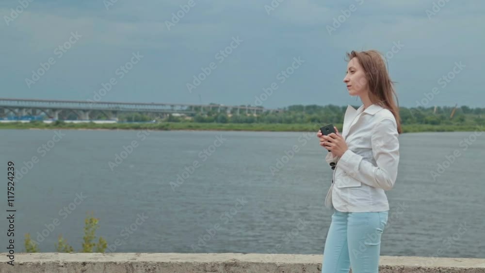 Beautiful girl standing on the embankment of the river with the phone, reads the message