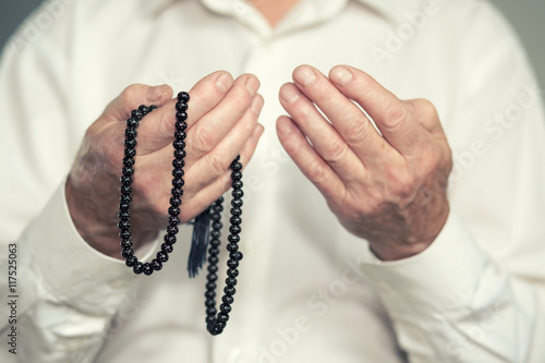 Praying hands of an old man holding rosary beads. Selective focus