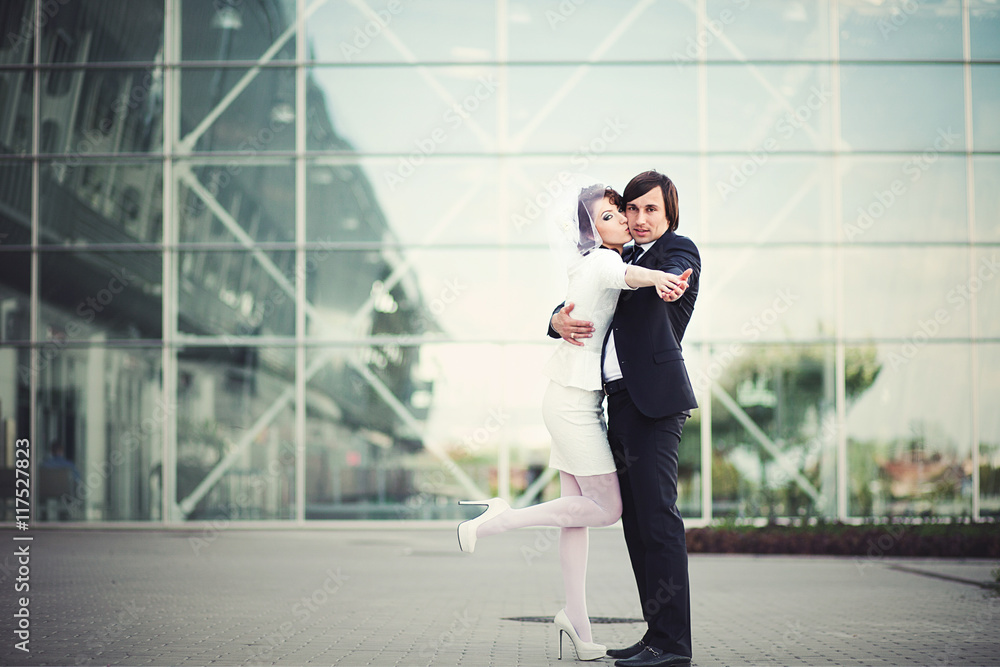 Wedding couple stands in the pose for a tango before a glass bui Wedding couple stands in the pose for a tango before a glass bui