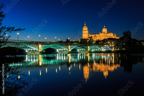 Night view of the Cathedral of Salamanca with Enrique Esteban bridge lit foreground and reflections in the Tormes river  Salamanca  Spain