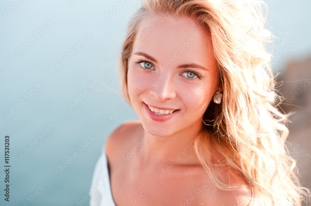 Naklejka premium Smiling blonde girl posing over sea background outdoors. Looking at camera. 20s.