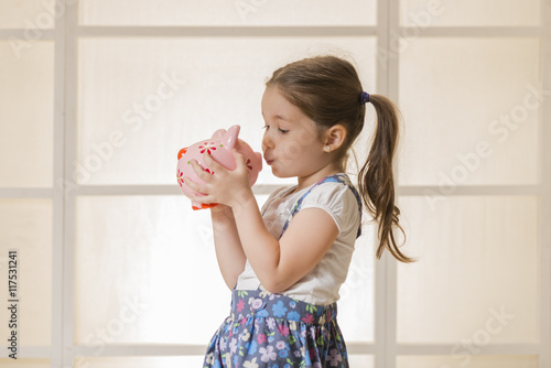 Portrait of happy young little girl kissing pink piggy bank. Education, school and money saving concept. Junior Savings Account concept
