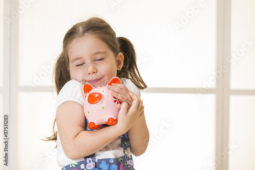Close up portrait of happy young little girl snuggling pink piggy bank. Education, school and money saving concept. Junior Savings Account concept