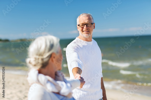 happy senior couple holding hands on summer beach