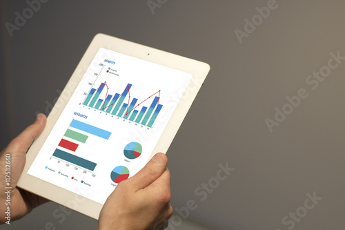 Hands holding white tablet with financial information displayed in graphical form on the screen.