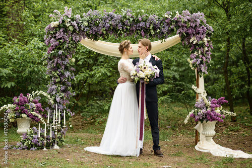  bride and groom near the arch of lilac in the woods.  young couple near the arch of lilac in the woods photo