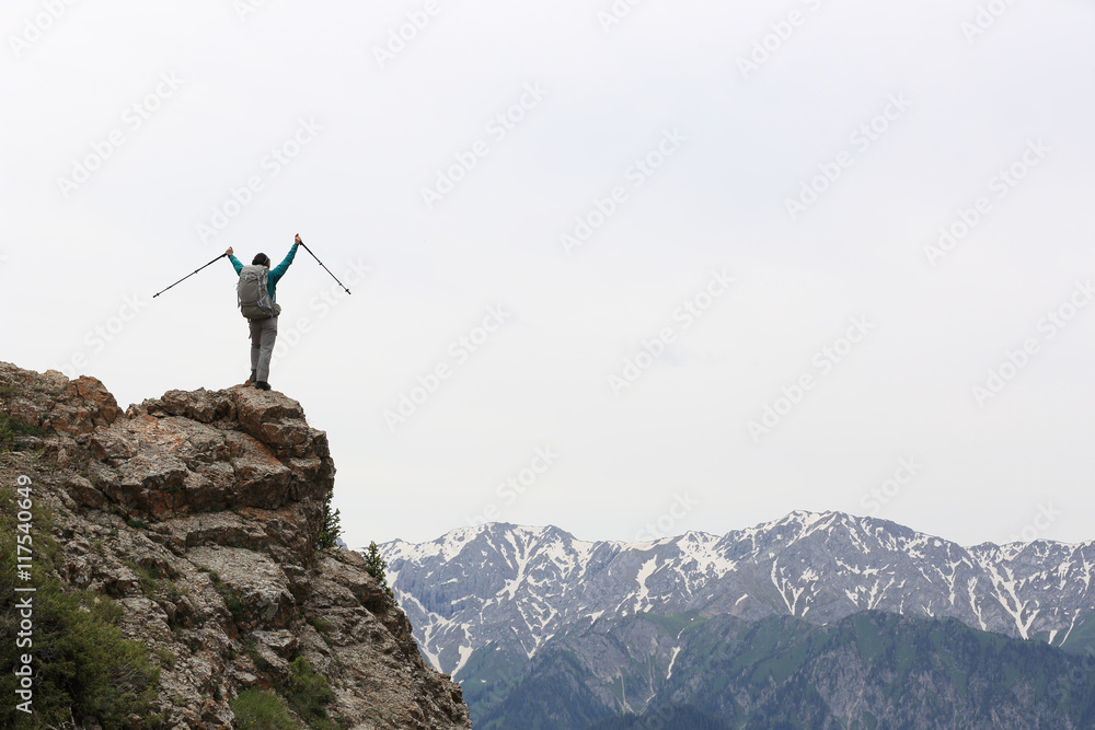 cheering young woman backpacker open arms on mountain peak cliff