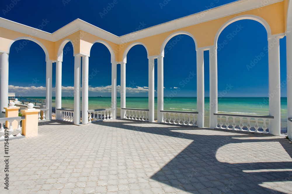 Rotunda with white columns on the embankment near the blue sea