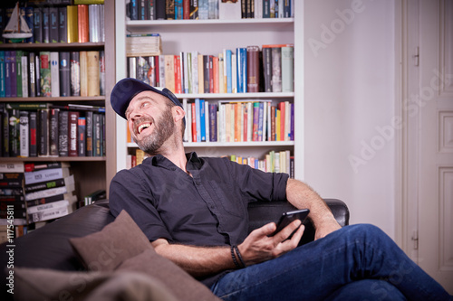 Man sitting in his living room with mobile phone laughing