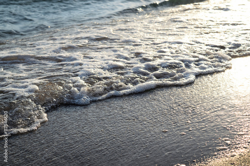 sandy beach and sea foam wave at sunset