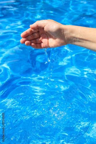 Hand of a girl taking water in the pool in summer. The water drips into the pool. © pablobenii