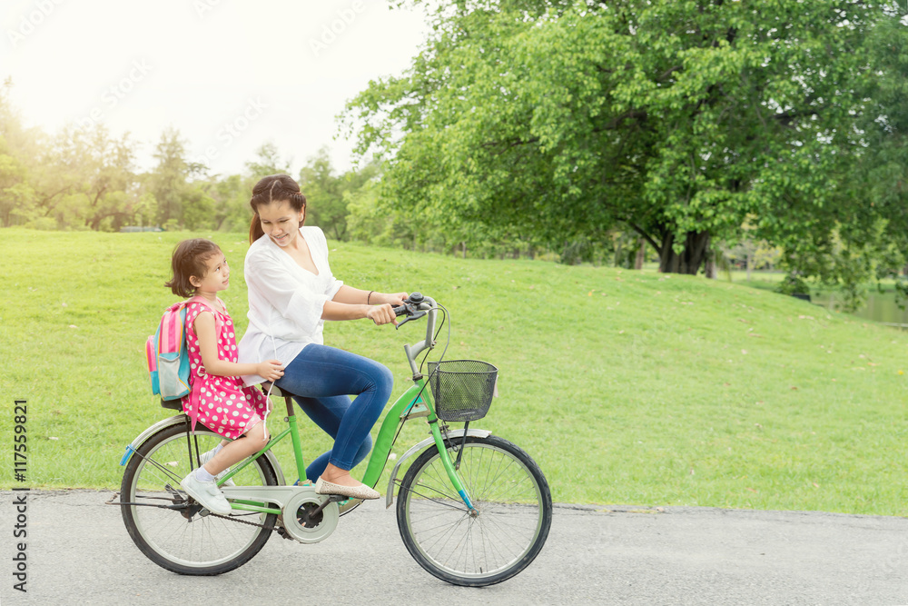 Asian mother and daughter cycling bicycle in park at school. Mot Asian mother and daughter cycling bicycle in park at school. Mot