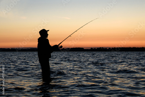 Fisherman silhouette at sunset on the lake while fishing 