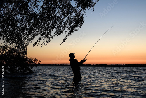 Fisherman silhouette at sunset on the lake while fishing 