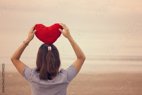 Woman holding a red heart on the beach