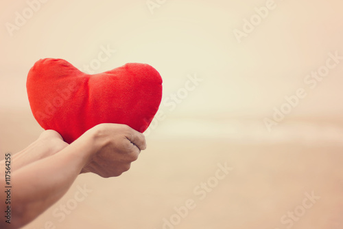 Woman holding a red heart on the beach