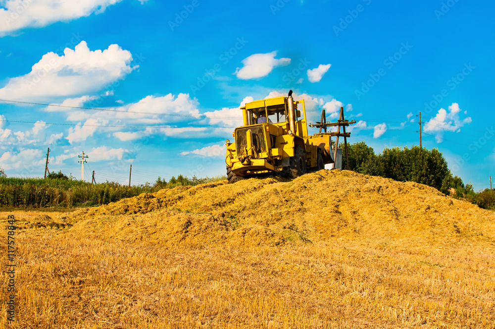 Fototapeta premium Yellow bulldozer in a field at harvest on a Sunny day
