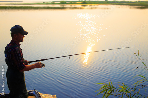 old fisherman throws a fishing rod spinning. the old man is fishing from a boat on the river at sunset