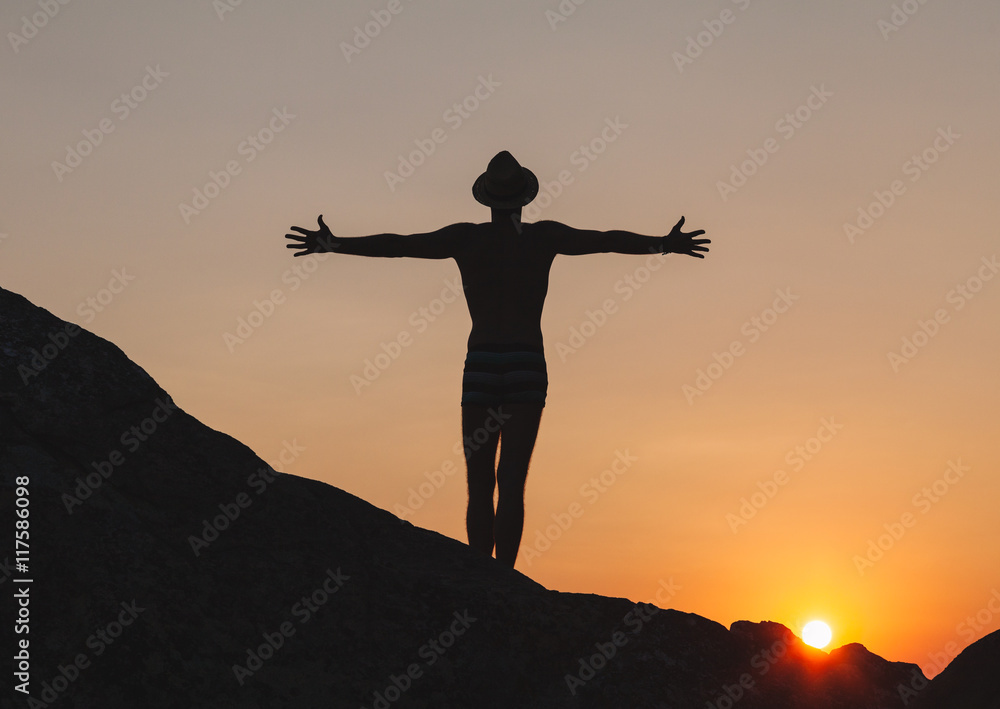 Silhouette of man raising hands in the sunset on the cliff