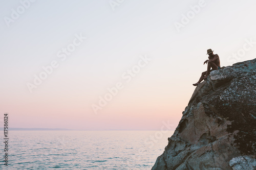 Man sitting on cliff top on the sunset over the sea