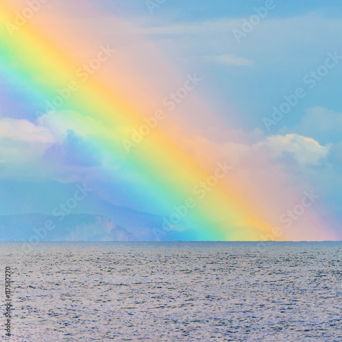 Scenic sky cloudscape with big bright rainbow above sea waves