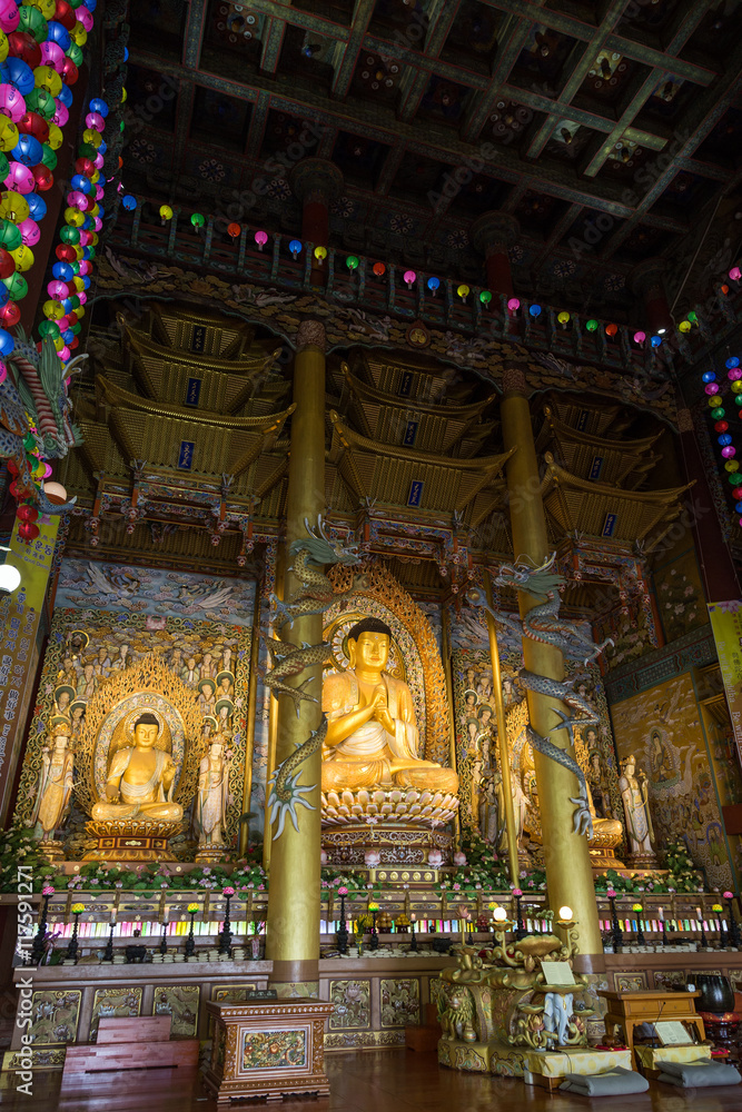 Tall Dharma Hall and three golden Buddha statues inside the Yakchunsa (Yakcheonsa) Temple on Jeju Island in South Korea.